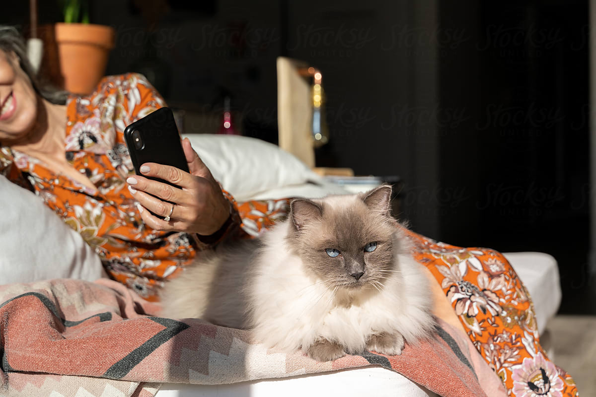 Mature woman using phone with cat at home