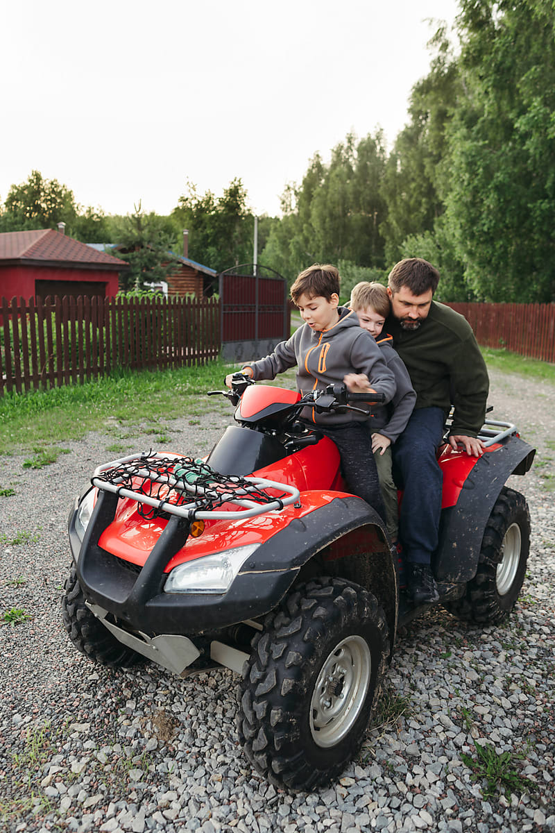 Little boys with dad on a quad bike in a rural area.