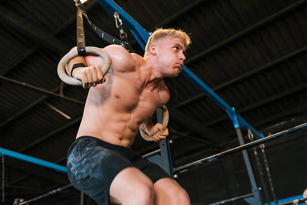 Athlete with athletic body hanging from gym rings