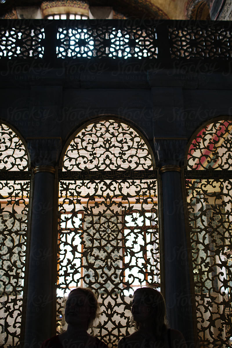 Two women\'s heads are silhouetted in front of a beautiful carved wooden screen.