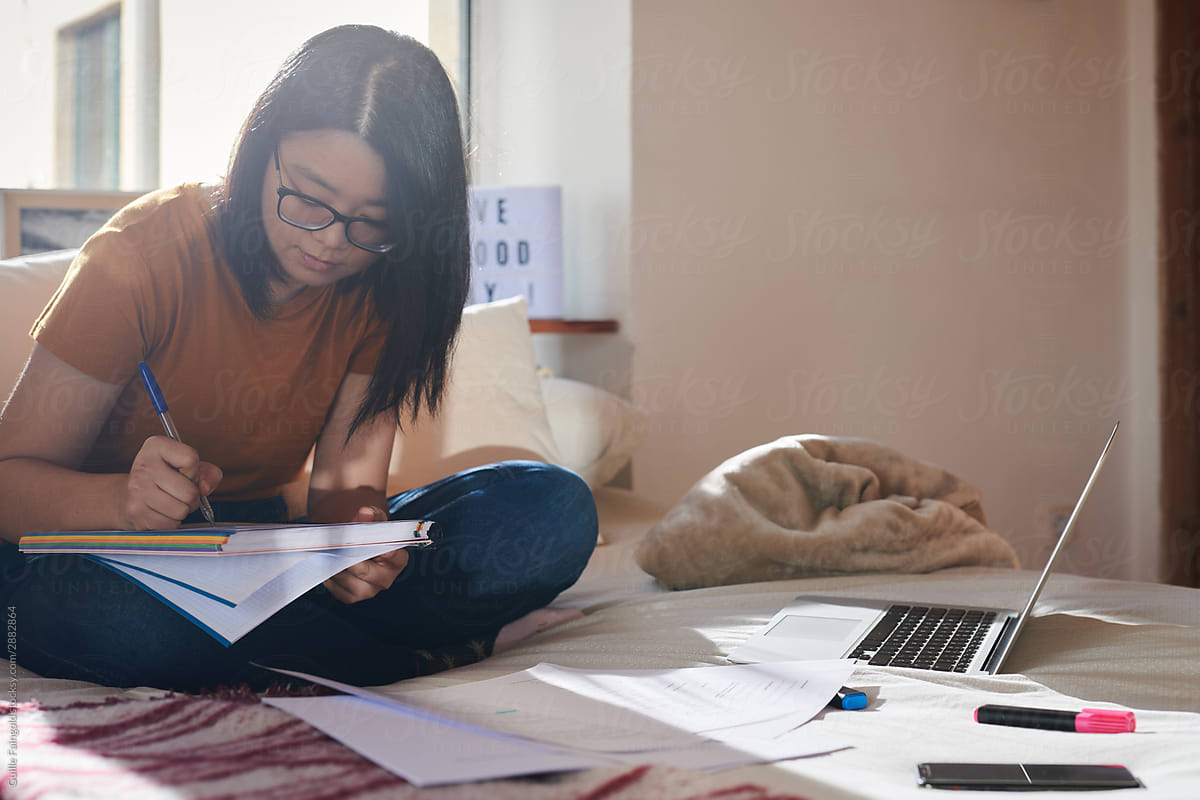 Smart student sitting on bed and writing in notebook
