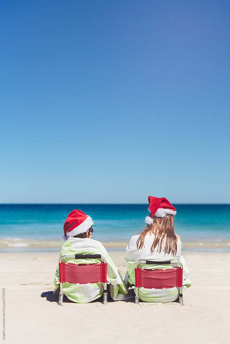 Two children sitting on red chairs at the beach on Christmas Day, viewed from behind