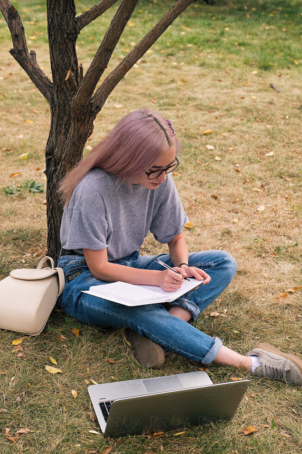 Clever busy woman with pink hair writing in notebook in park