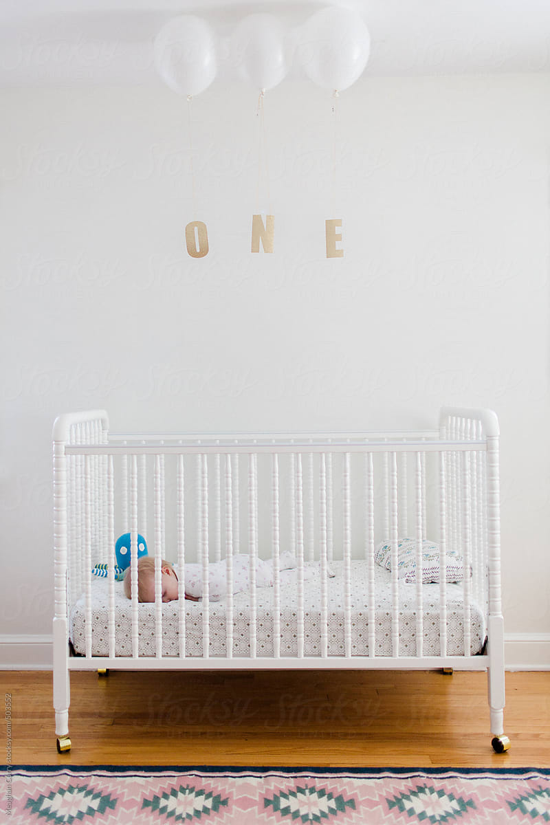 baby asleep in her crib on her first birthday with balloons and the word one