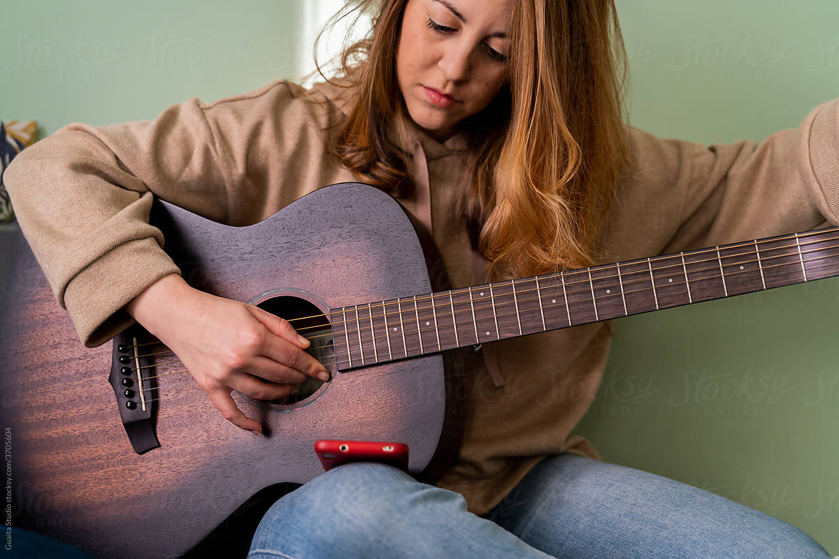 Woman tuning guitar with phone