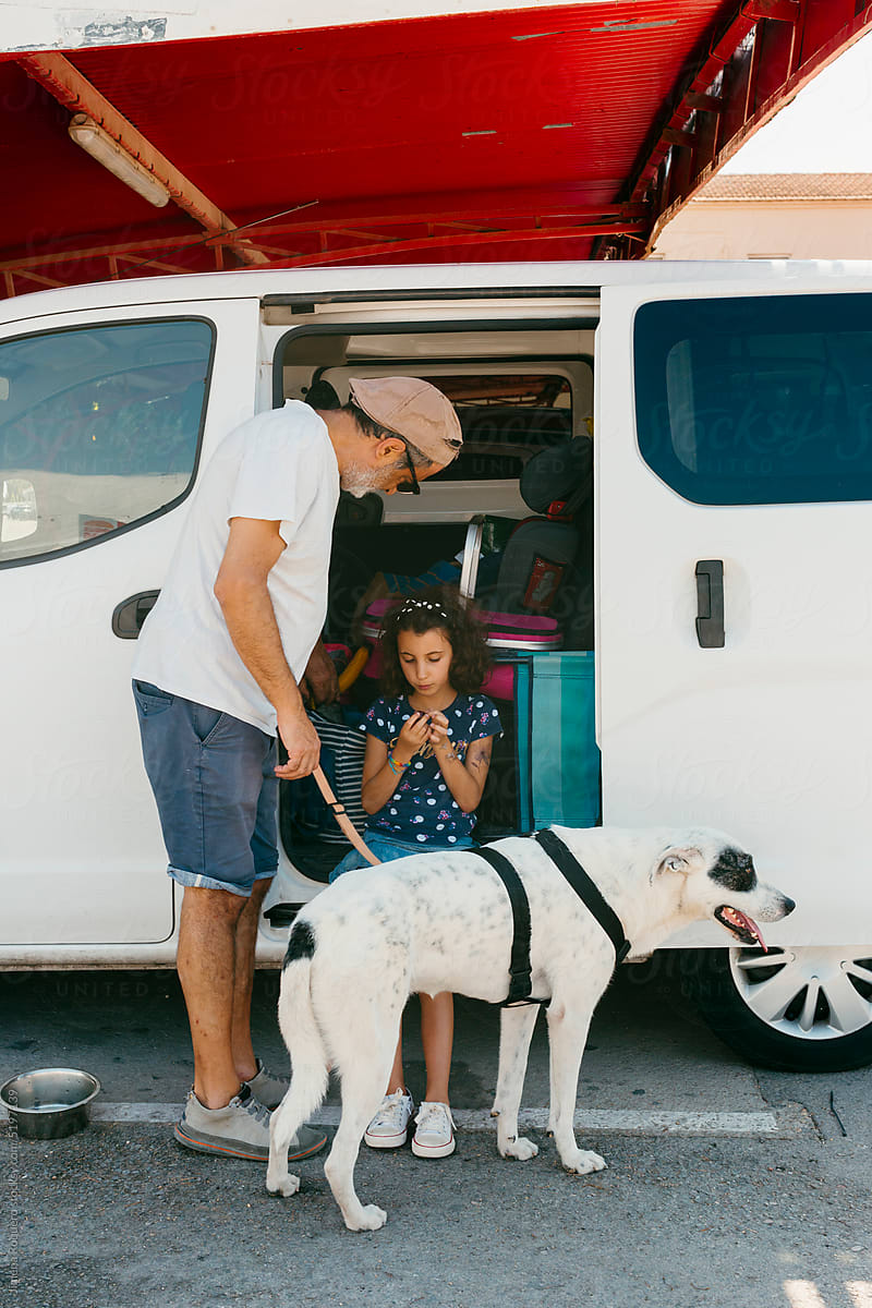 Man, kid and dog on in road trip stop standing by van\'s open door