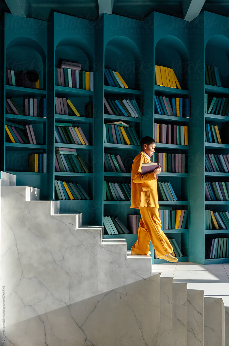 Woman in yellow suit going down stairs in room with book shelves