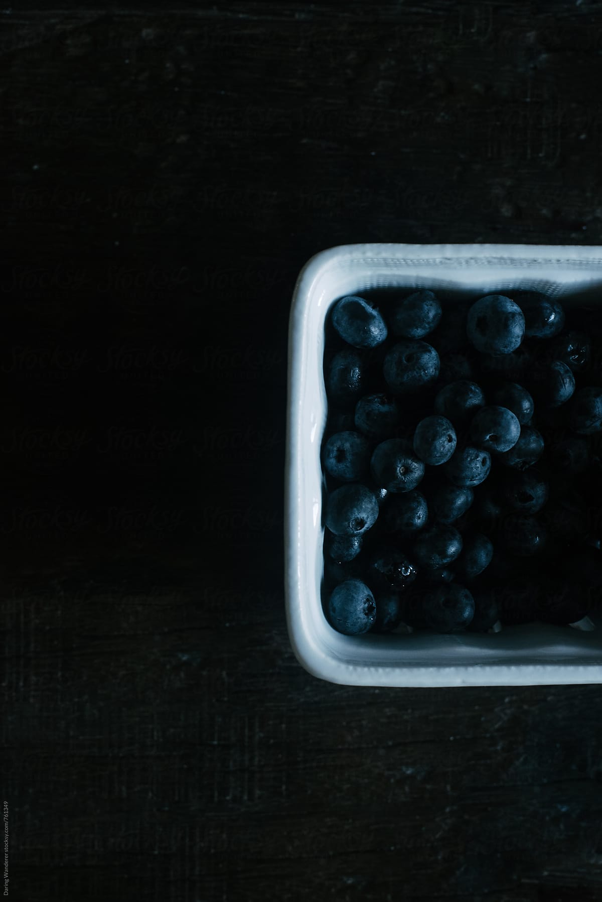 Dark and moody shot of blueberries in porcelain container on dark wood table