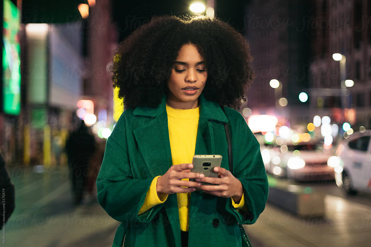 Black woman using smartphone walking through the city at night