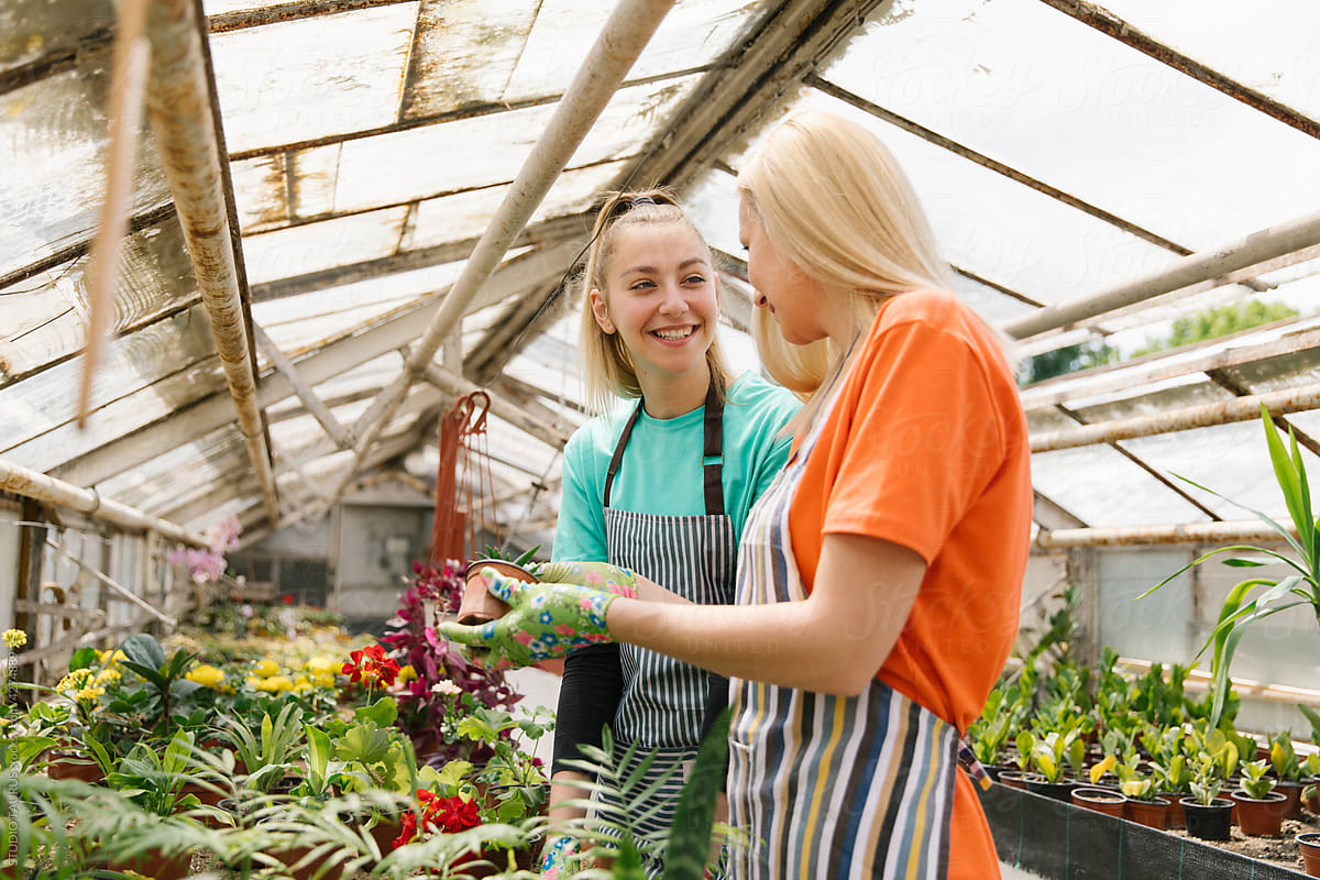 Mother And Daughter Nurturing Plants In Greenhouse