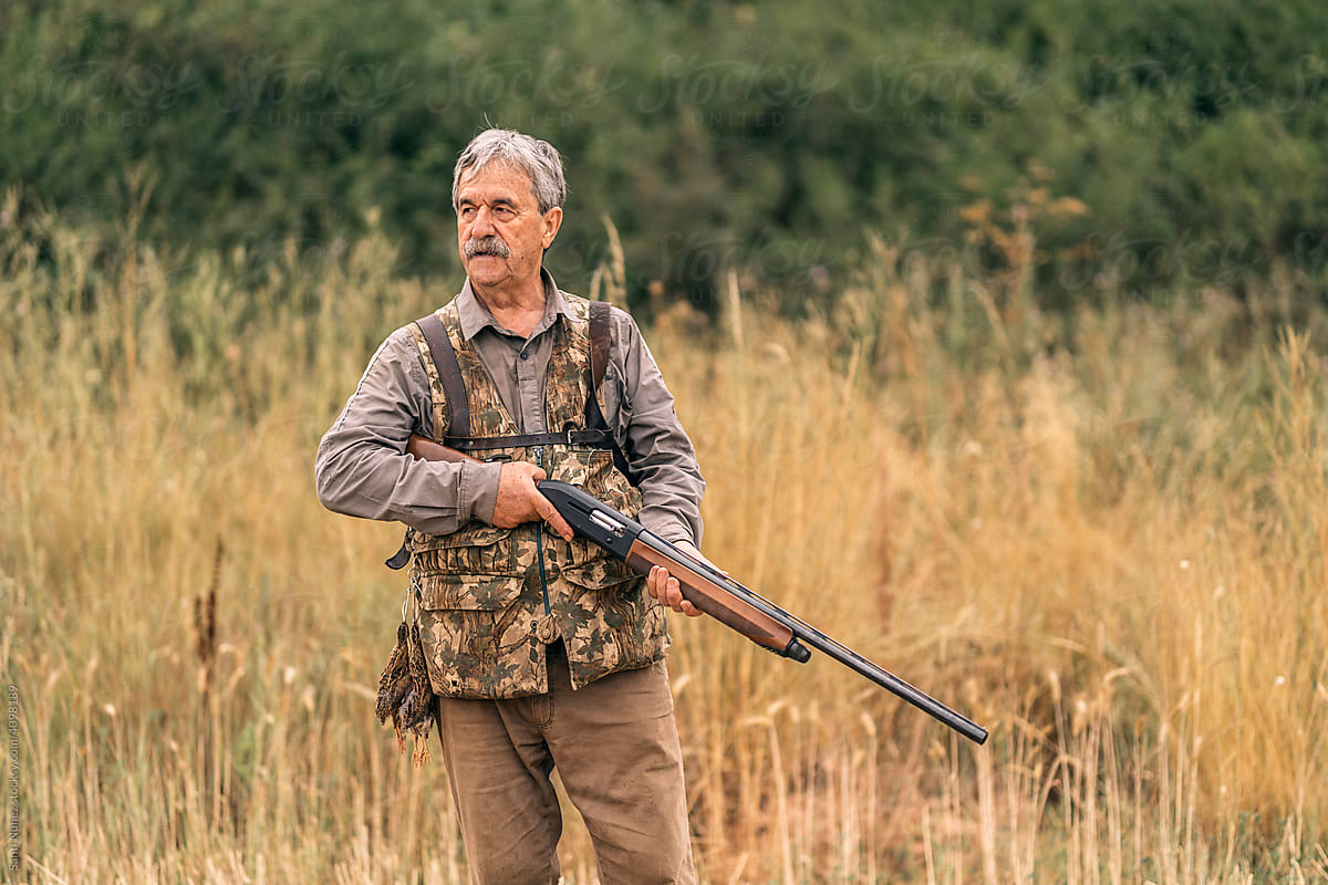 Mature hunting man holding a gun while searching for new preys.
