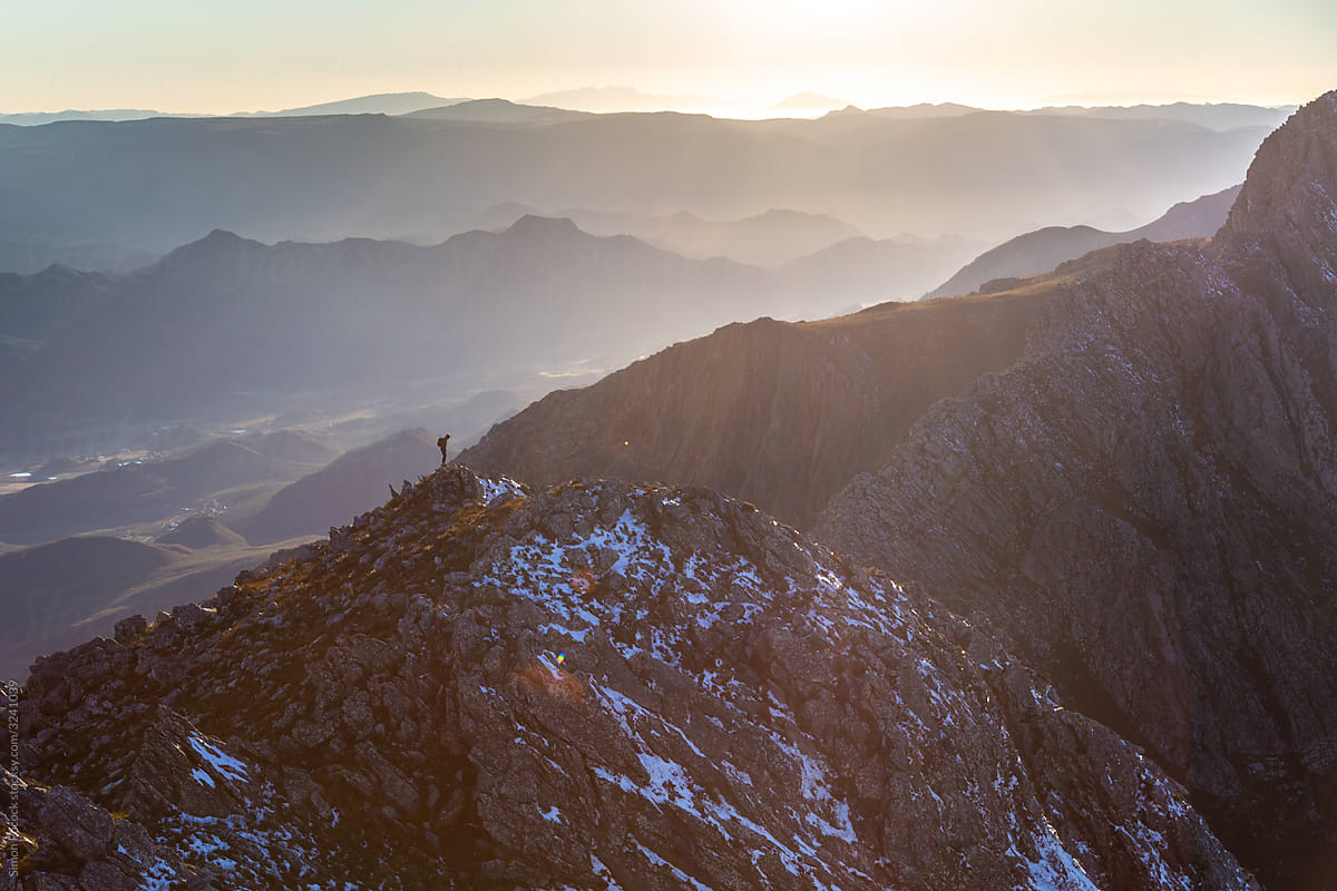Lone Hiker standing on a peak as the sun rises over the mountains in the distance
