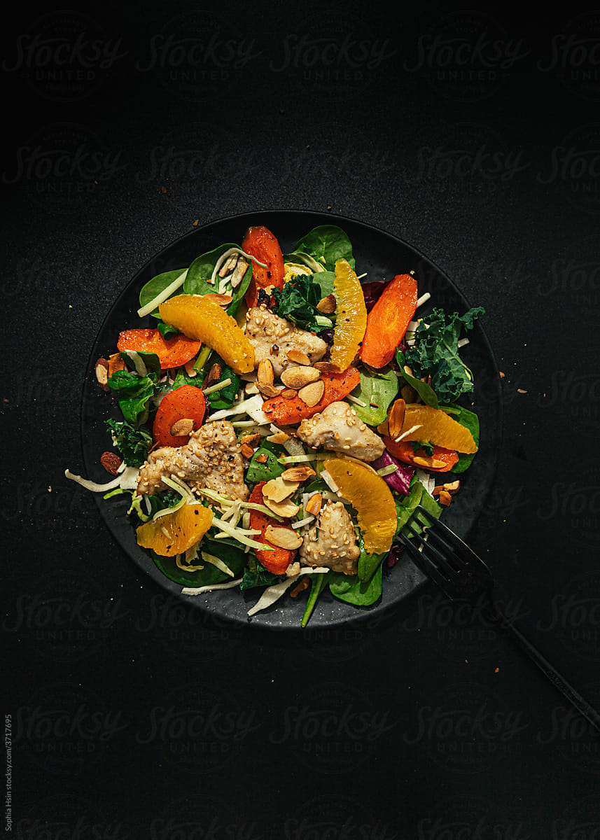 Sesame chicken salad with orange slices on dark background