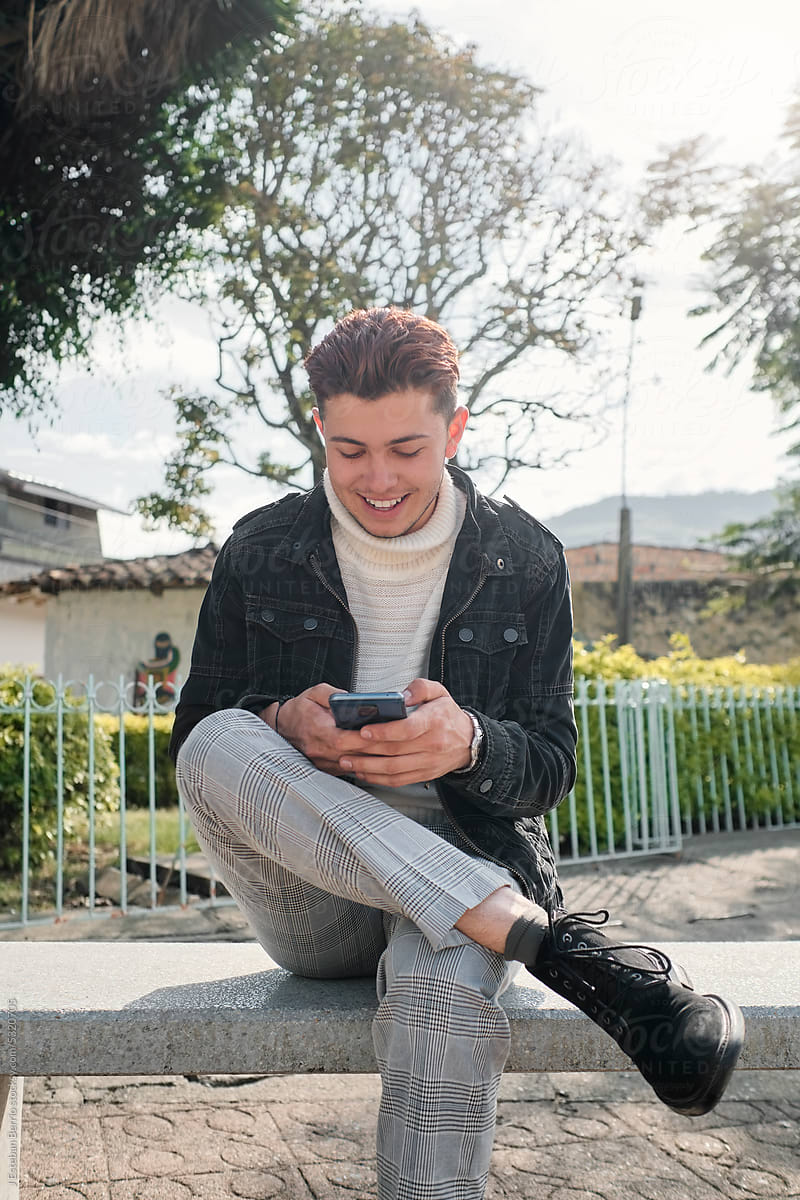 Portrait of a young Latino man looking at memes on his phone