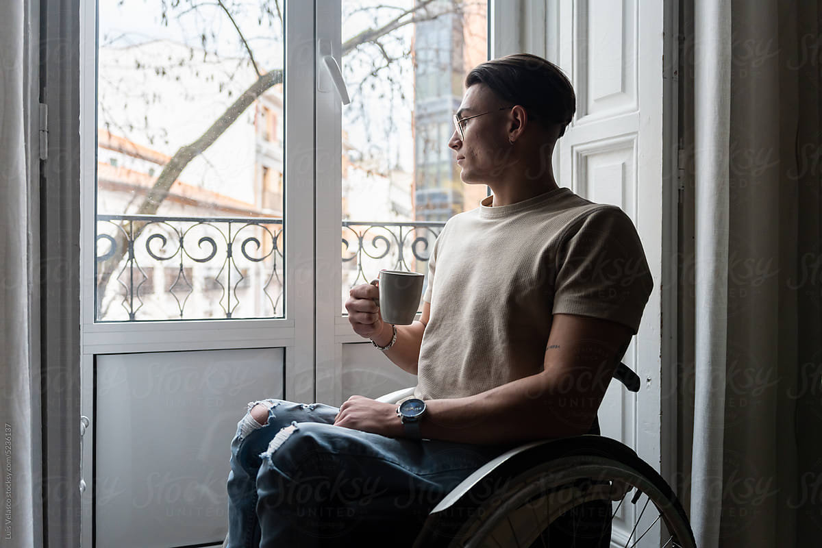 Young Man User Of A Wheelchair Looks Out The Window