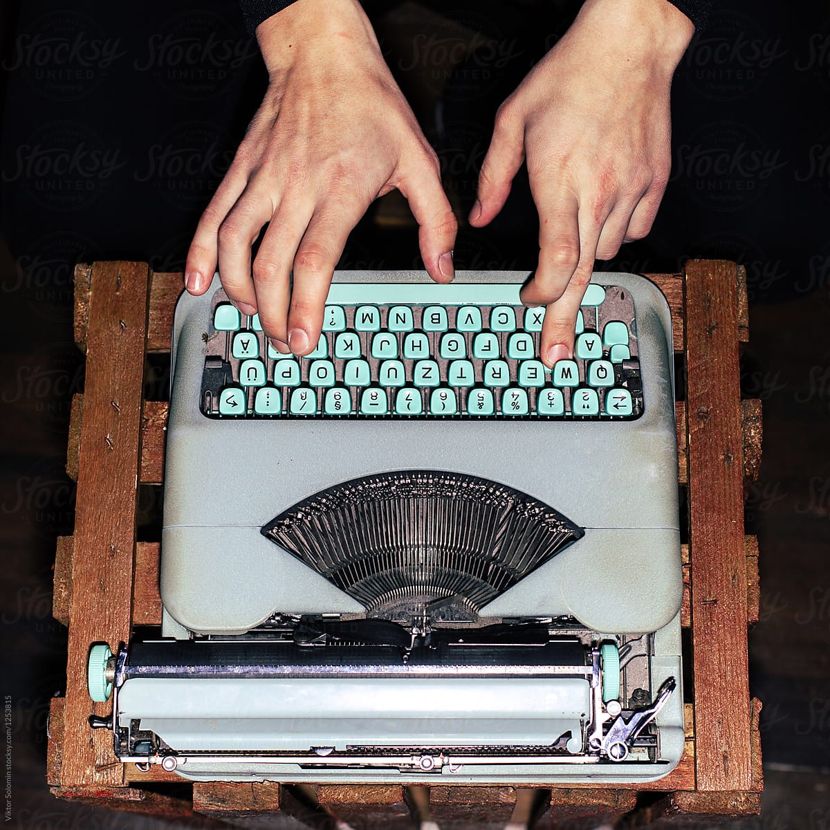 Hands closeup typing on blue vintage typewriter standing on wooden box