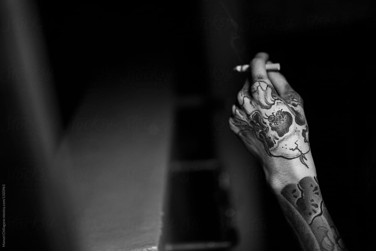 Young Japanese man with a tattoed hand holding a lit cigarette