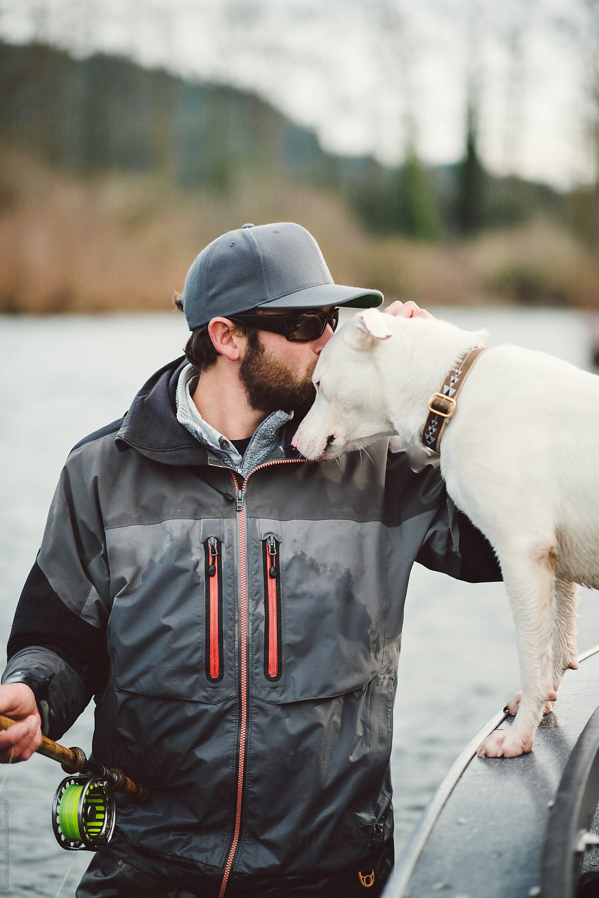 Fly fisherman embracing his dog while standing in a river fishing.