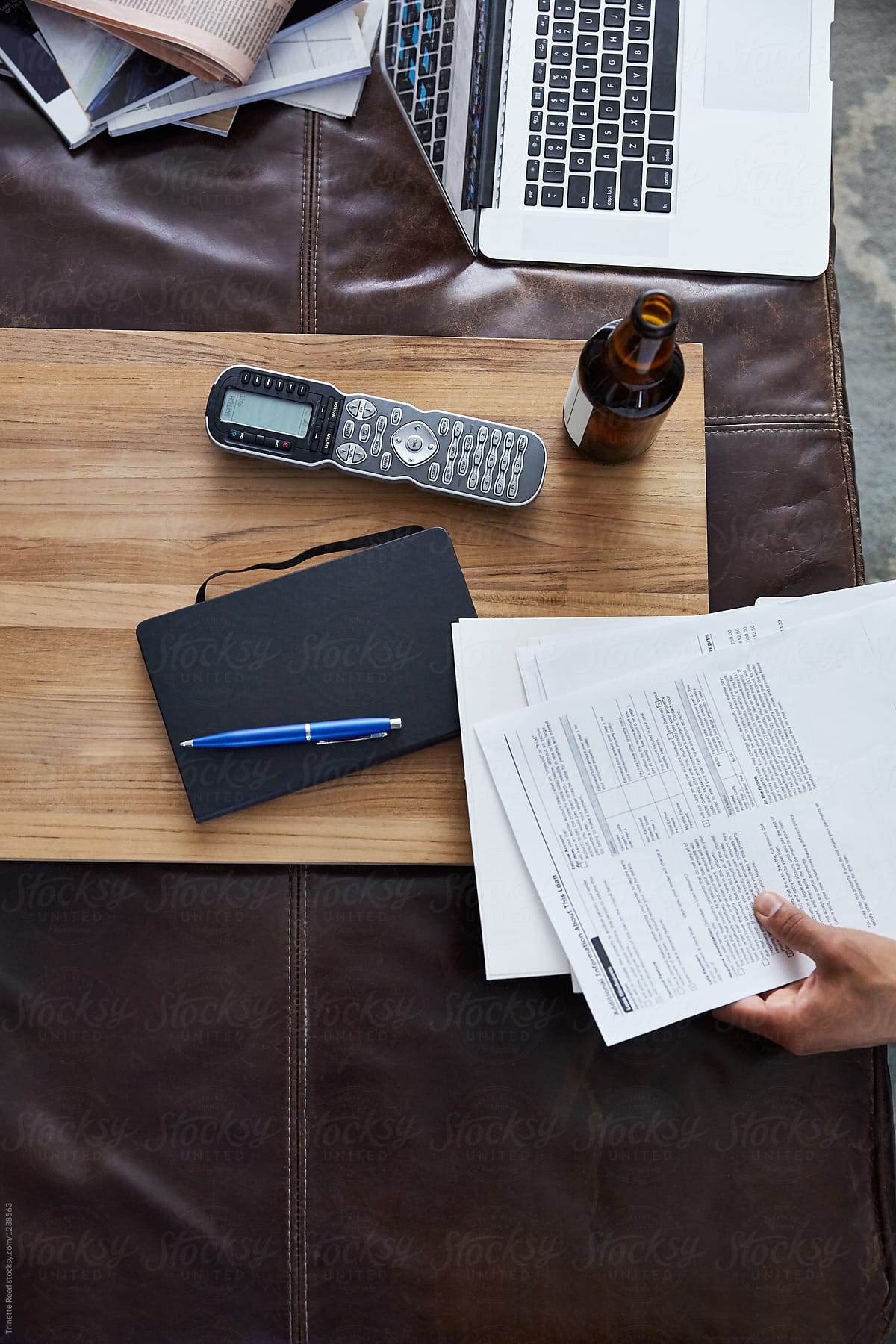 Mortgage contract with laptop, beer, notebook, and remote control in living room.