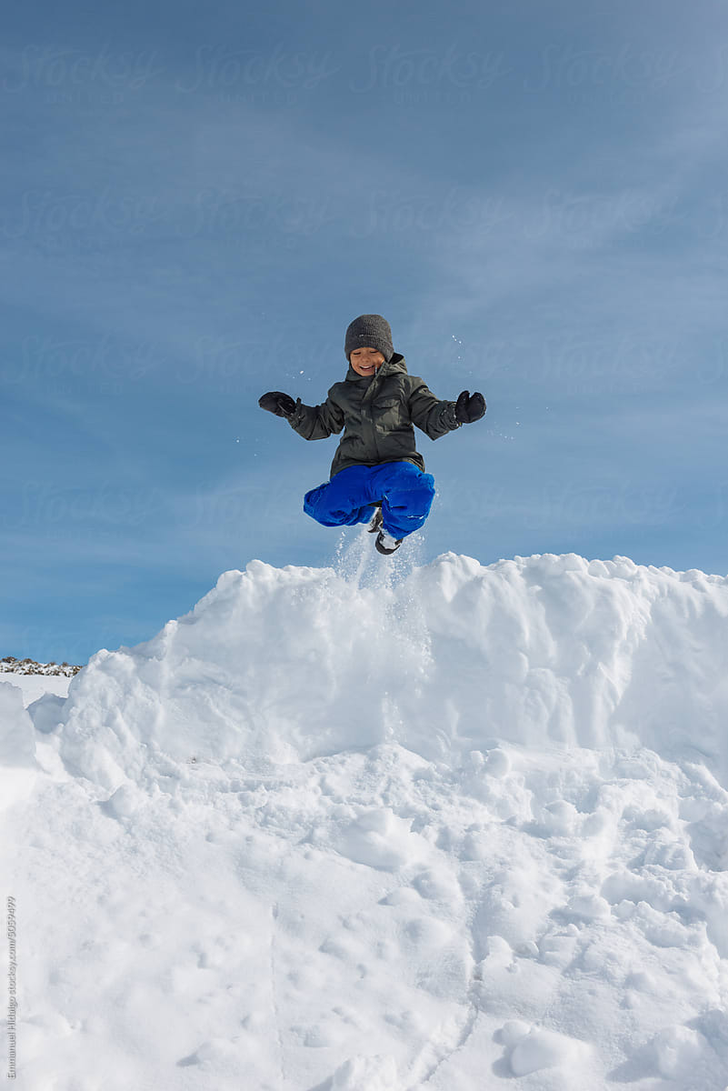 Young adventurous boy jumping off a snow bank