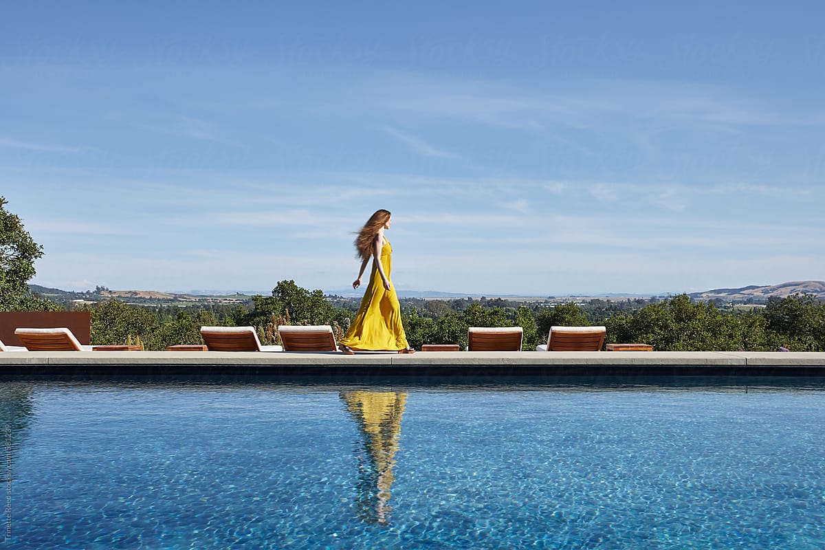 Fashion image of woman walking by luxury pool  in dress