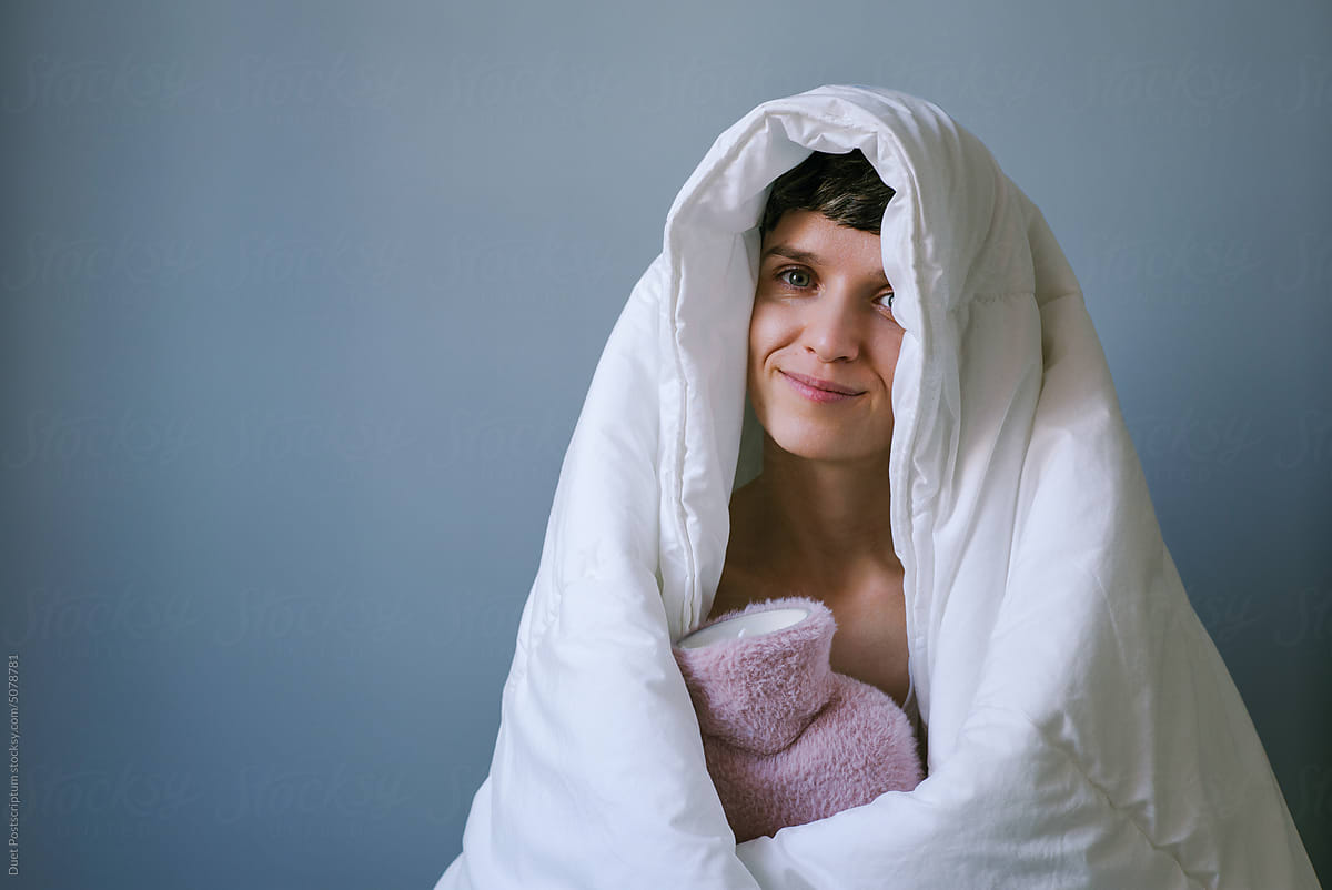 Young woman wrapped in a warm blanket with a water heating pad.