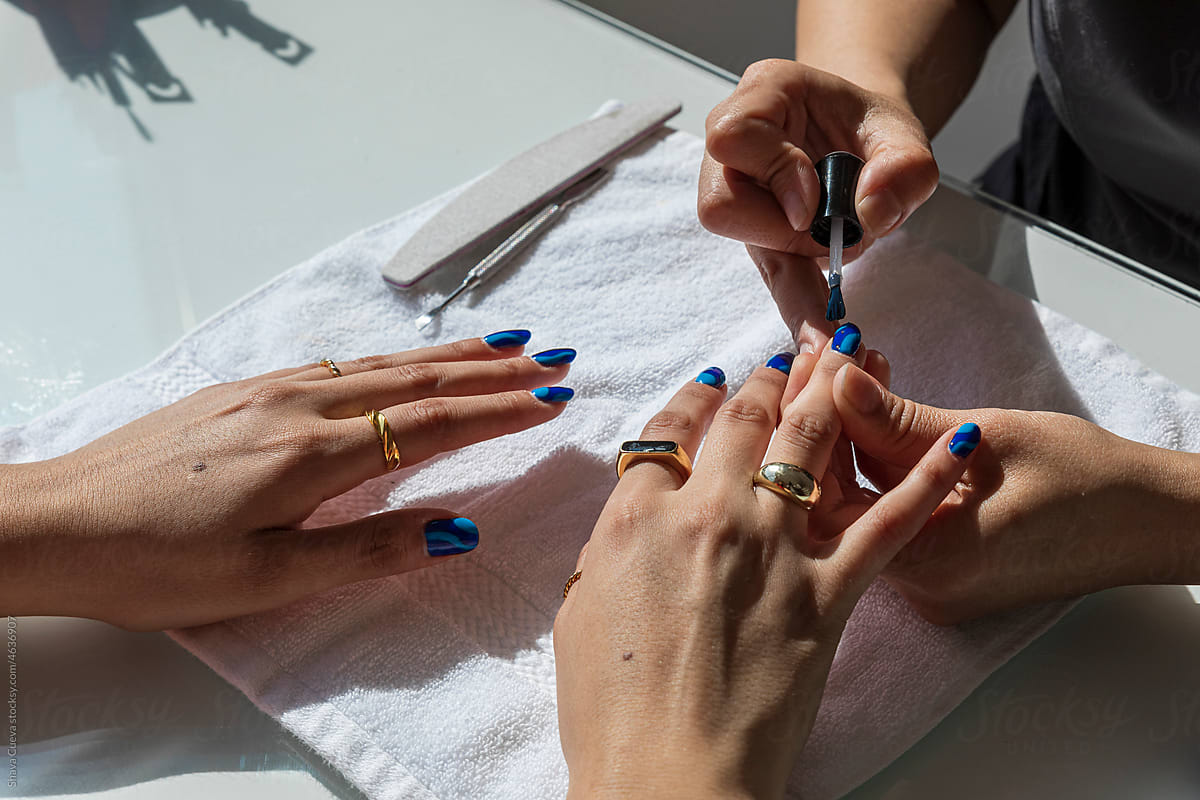 Woman painting blue nails on another woman with gold rings