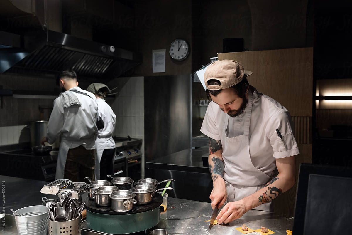 Male cook cutting pasta dough near colleagues
