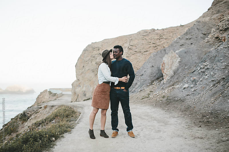 woman kisses and holds man on path in front of rocky landscape