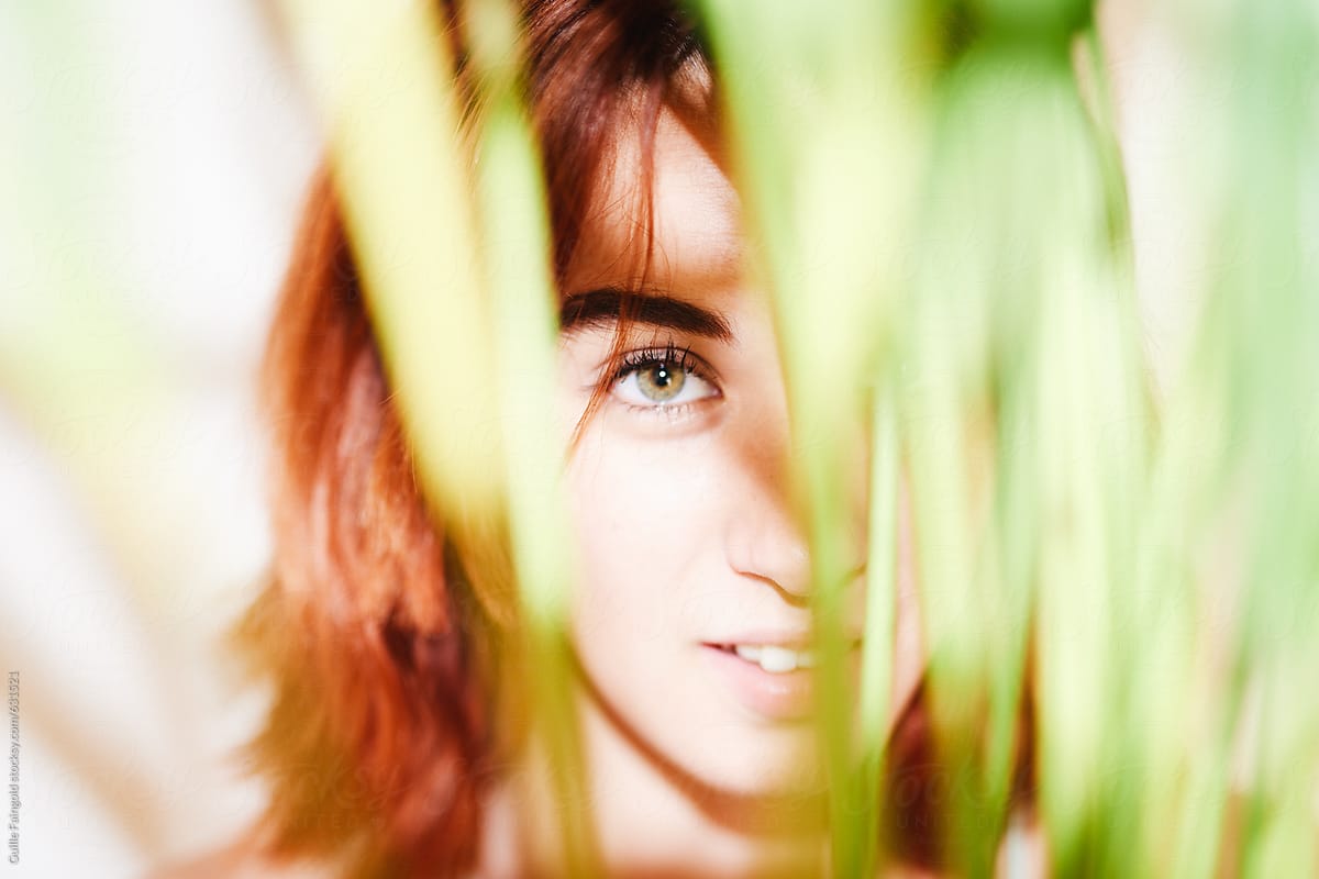 Young woman hiding behind plant leaves