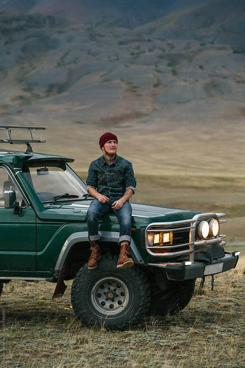 Young man sitting on the old green jeep parked in wild area