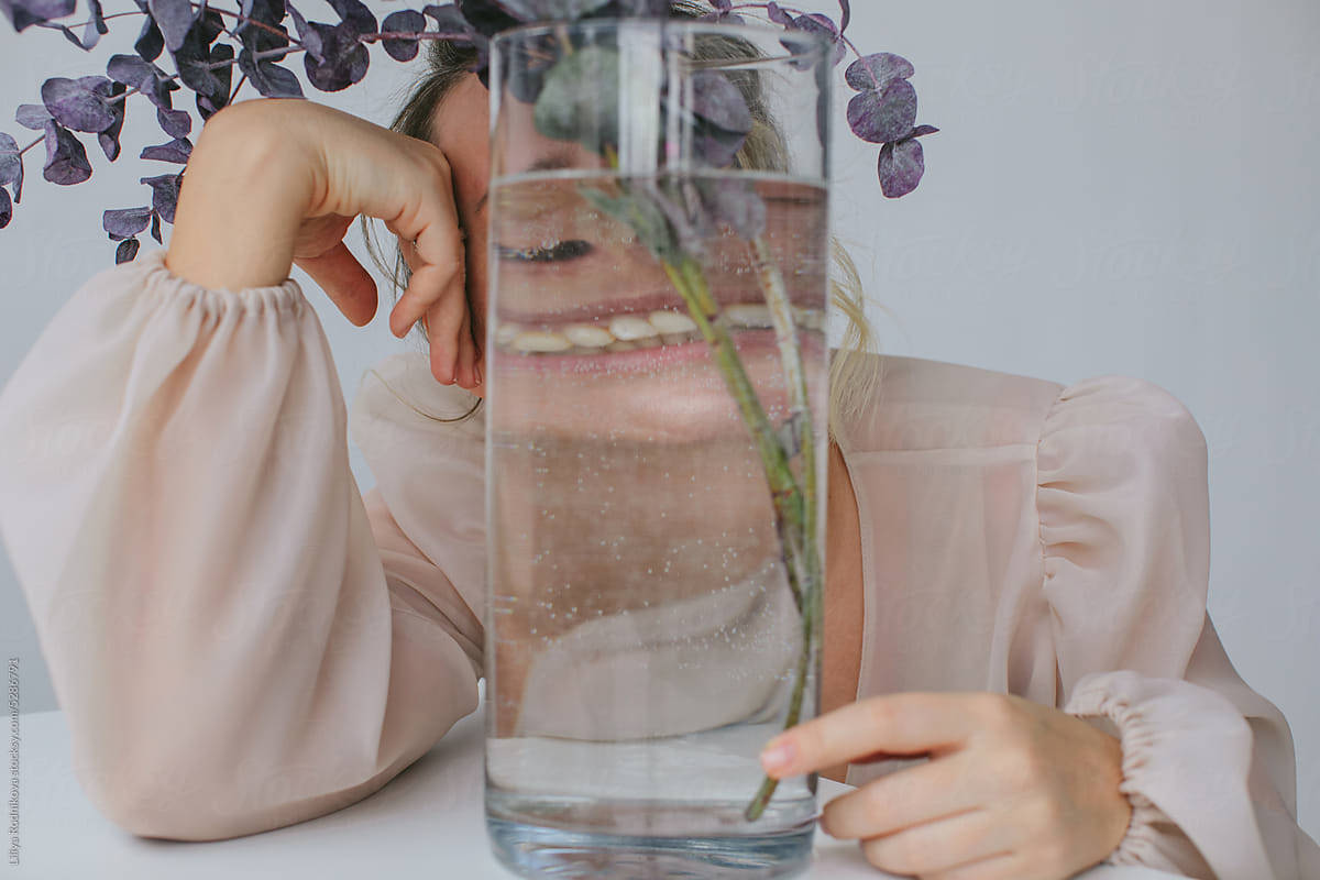 Anonymous woman smiling behind glass vase