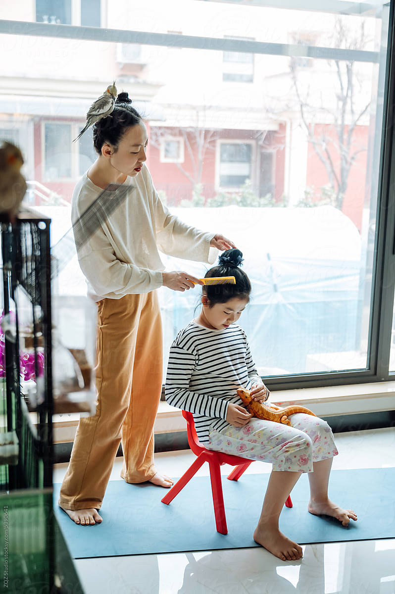 Mother styling hair of daughter at home with pets