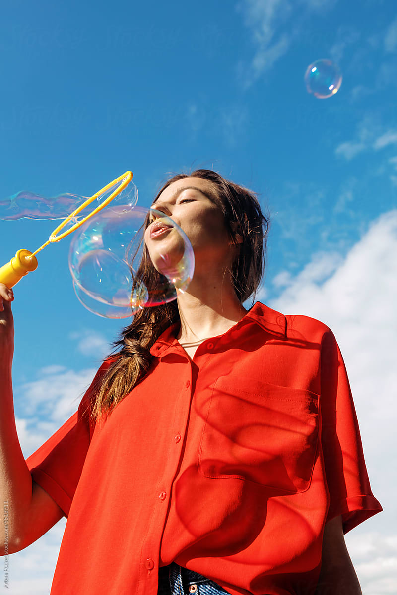 A young woman in a red shirt blows soap bubbles. Summer portrait