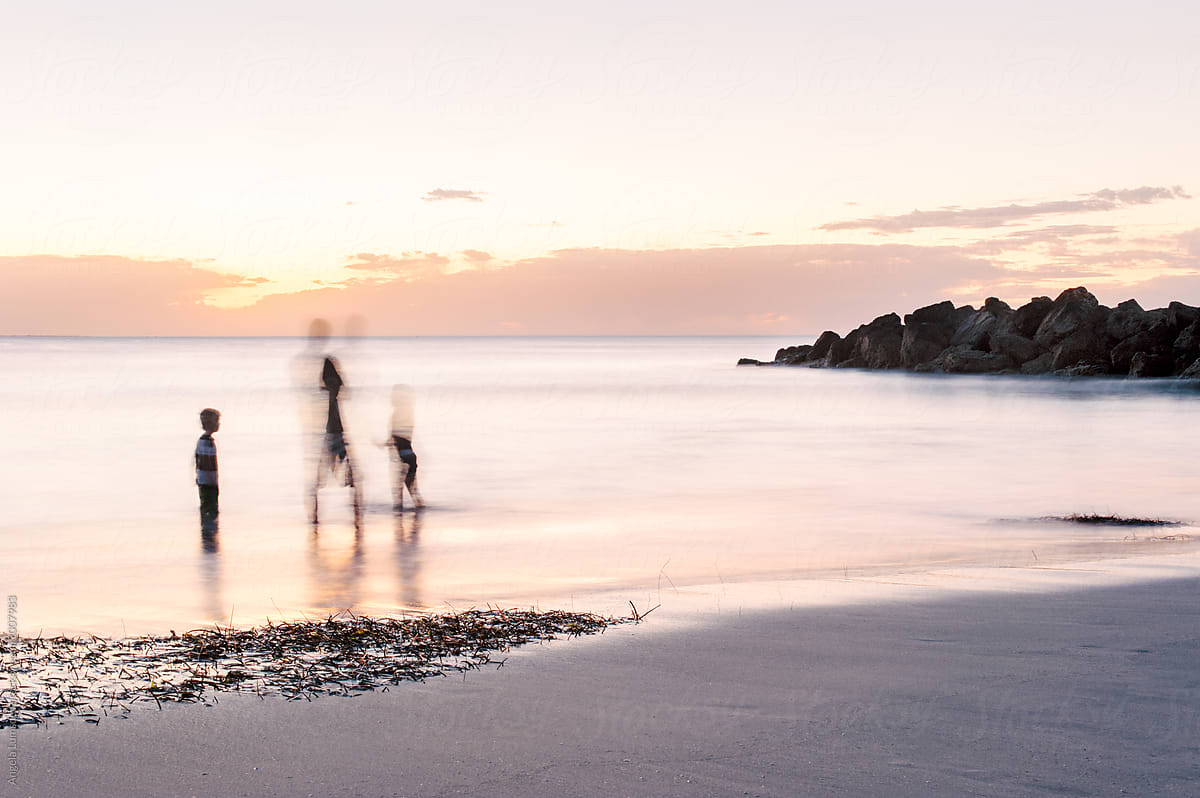 Family playing in water at the beach at sunset in summer