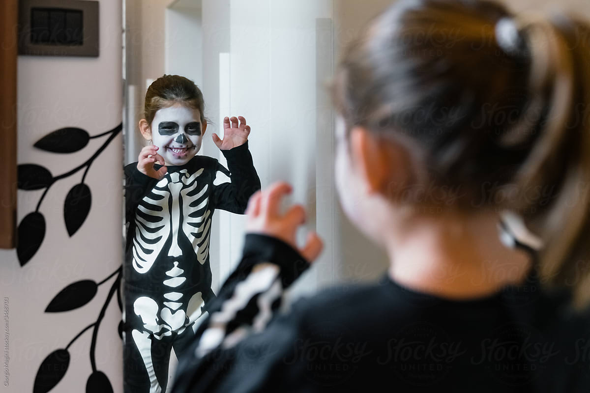 Little girl in skeleton costume near mirror