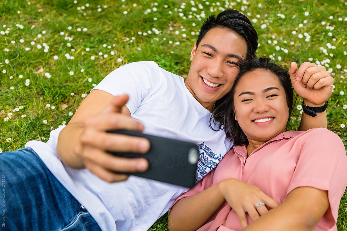 «young Filipino Couple Taking A Selfie While Lying Down On Grass Del