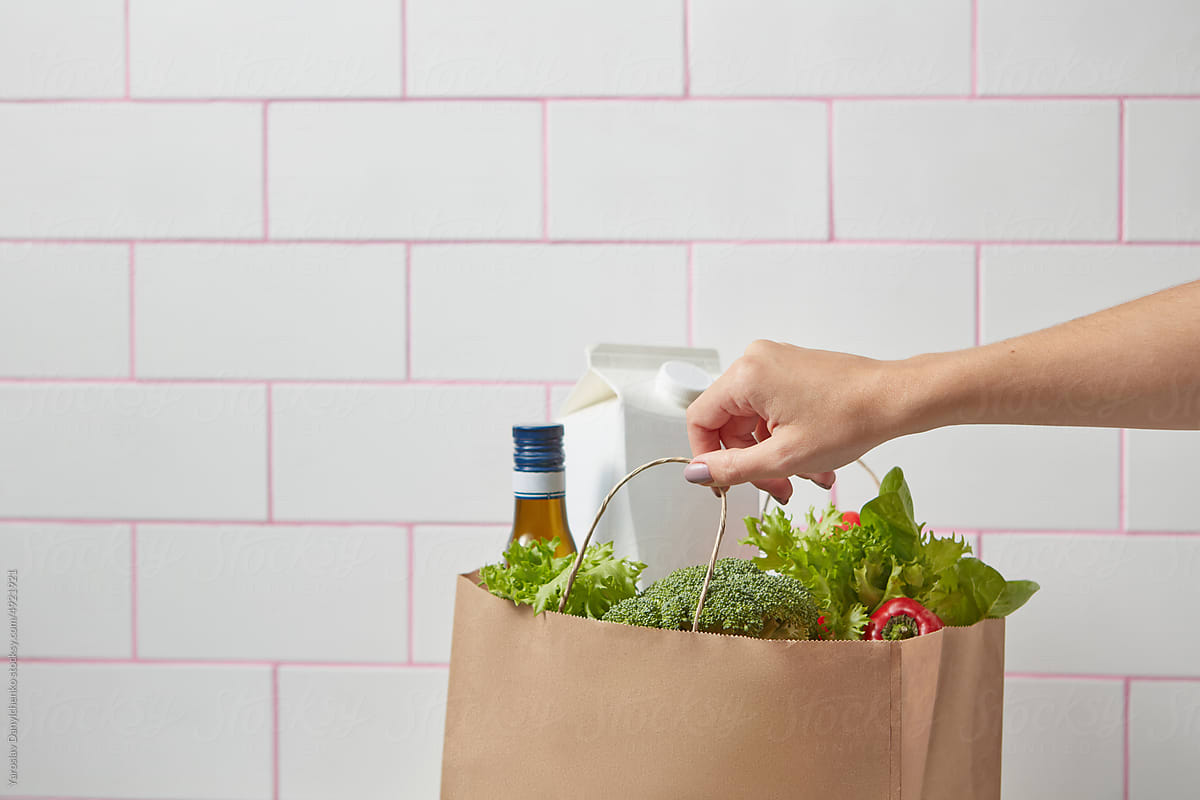 Groceries in paper bag held by woman\'s hand.