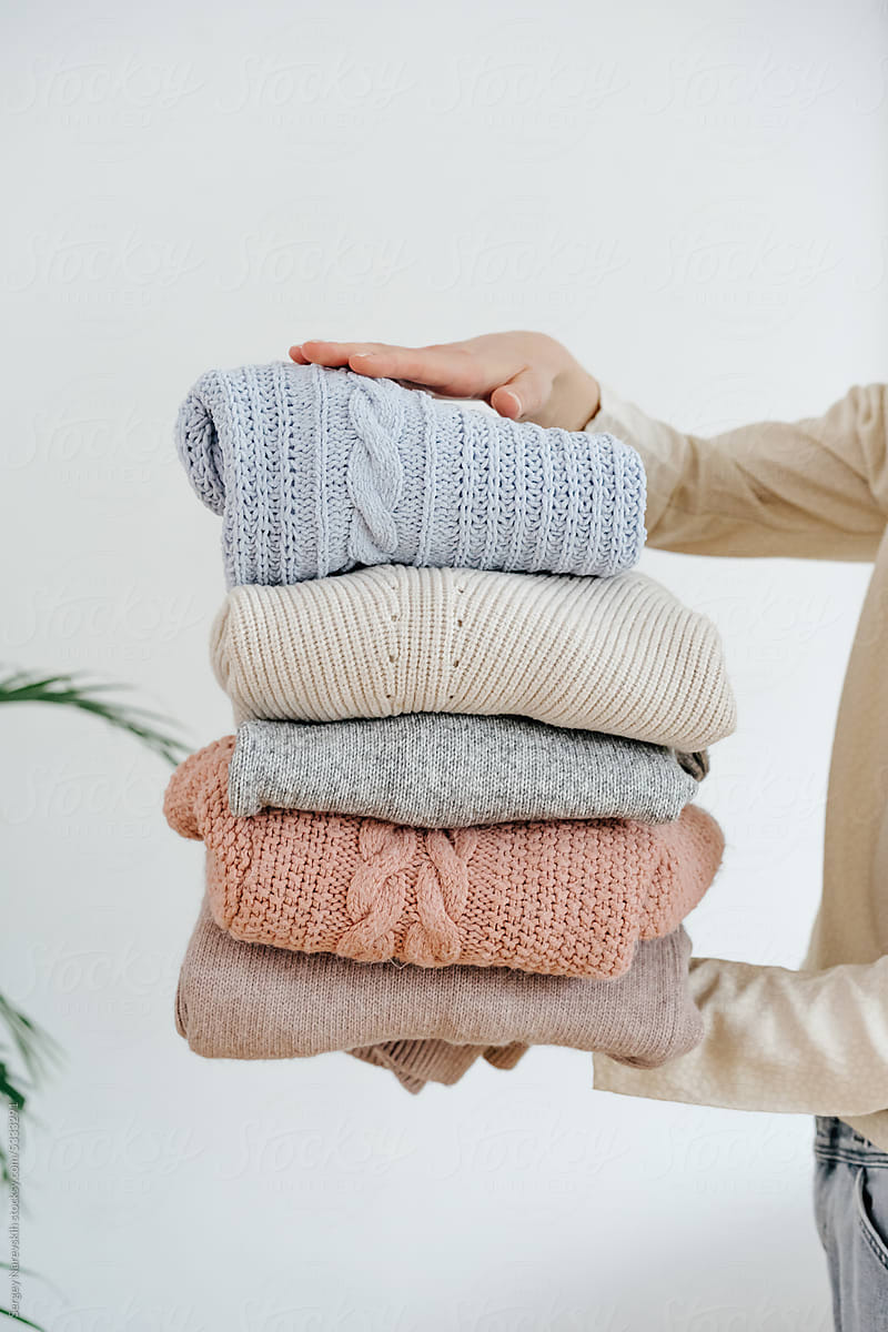 Crop female holding stack of various sweaters