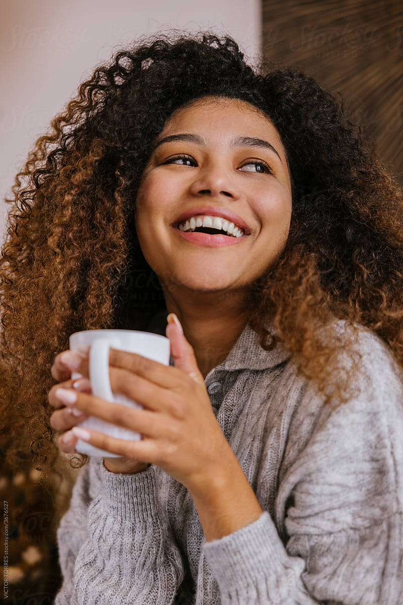 Young black woman with cup of coffee resting on sofa