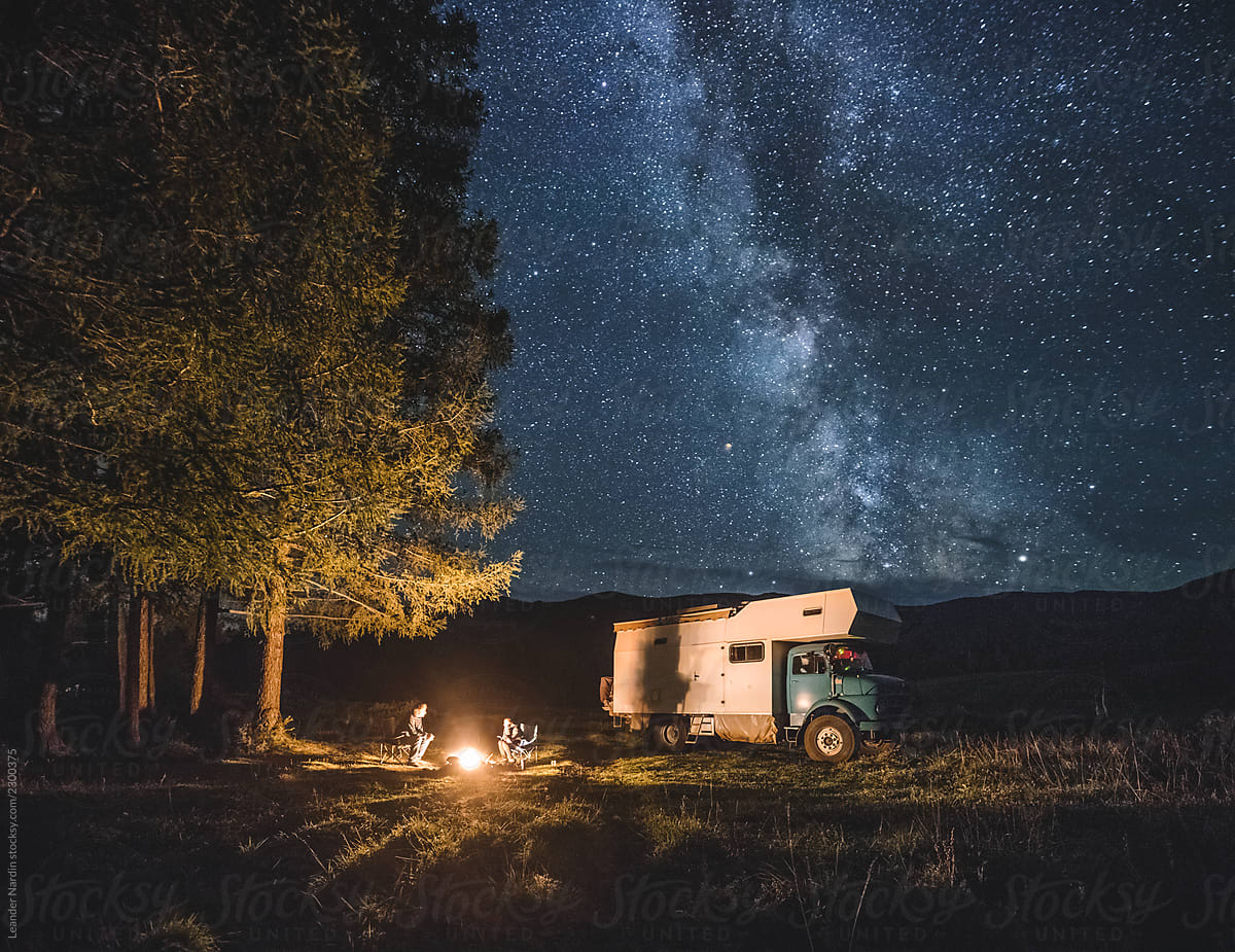 family with camping truck sitting at a campfire in russian altai under the milky way