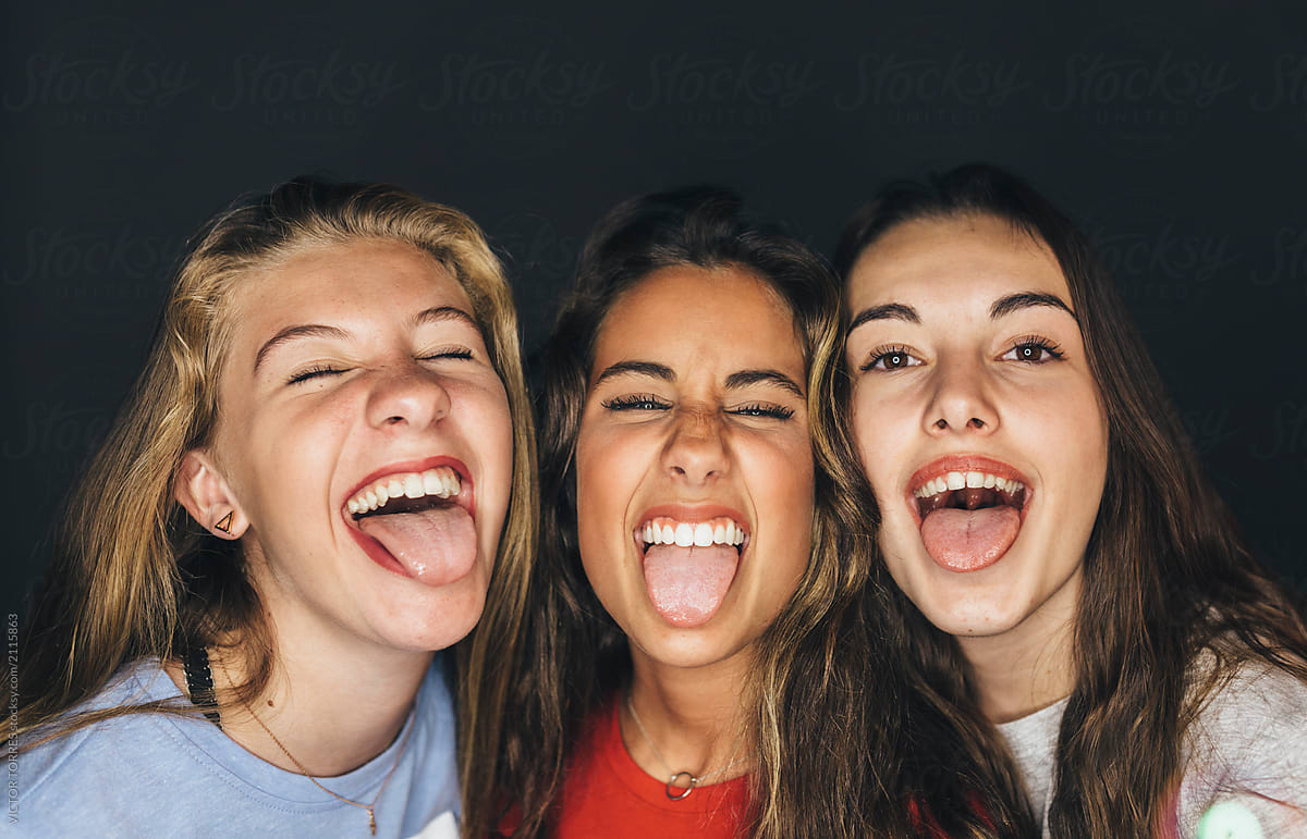 Studio Portrait Of Cute Teen Girls Sticking Out Tongue by Stocksy