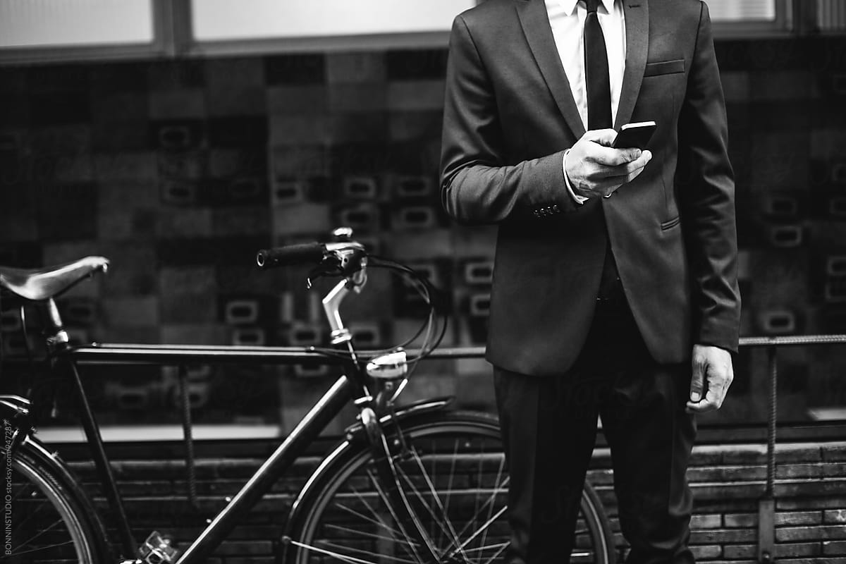 Closeup of a businessman using his phone next to bicycle on the street.