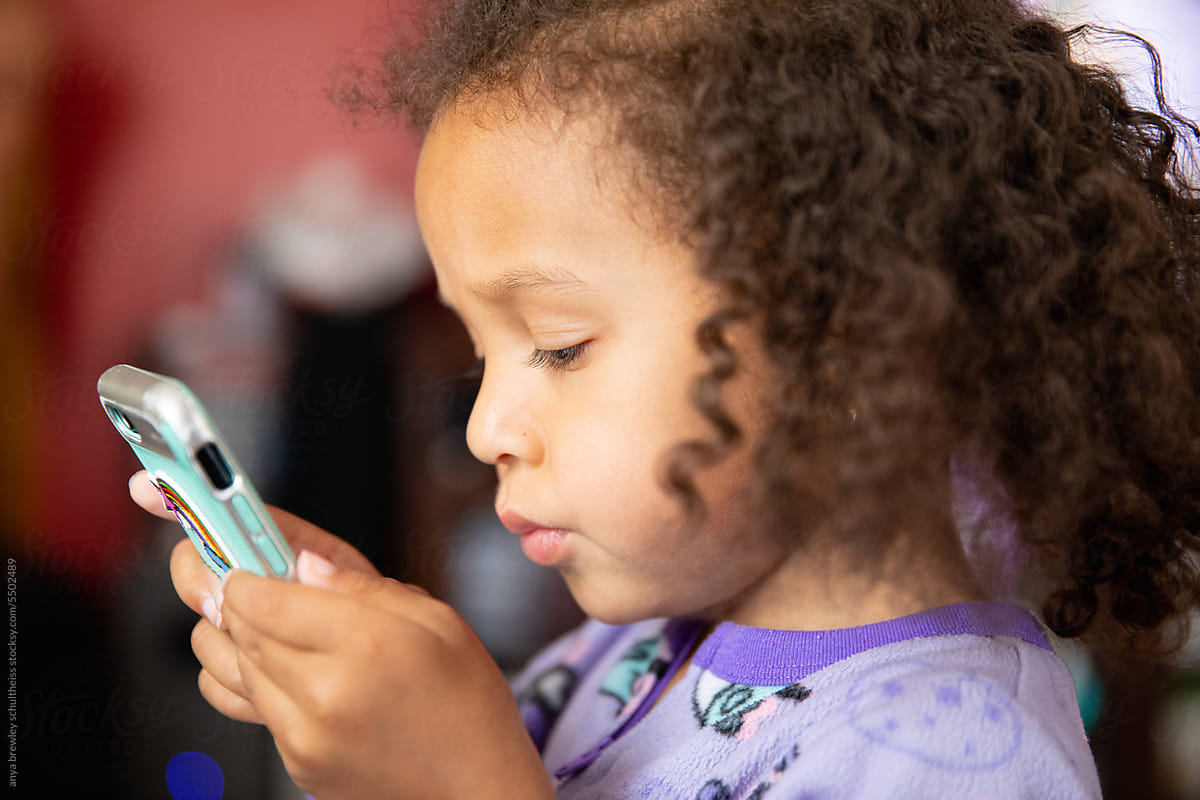 Preschool child with curly hair using an electronic phone