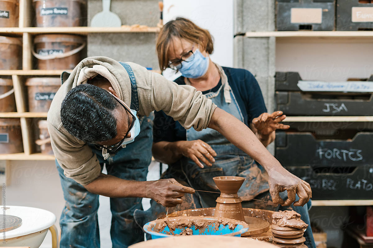 Black potter helping apprentice to cut vase