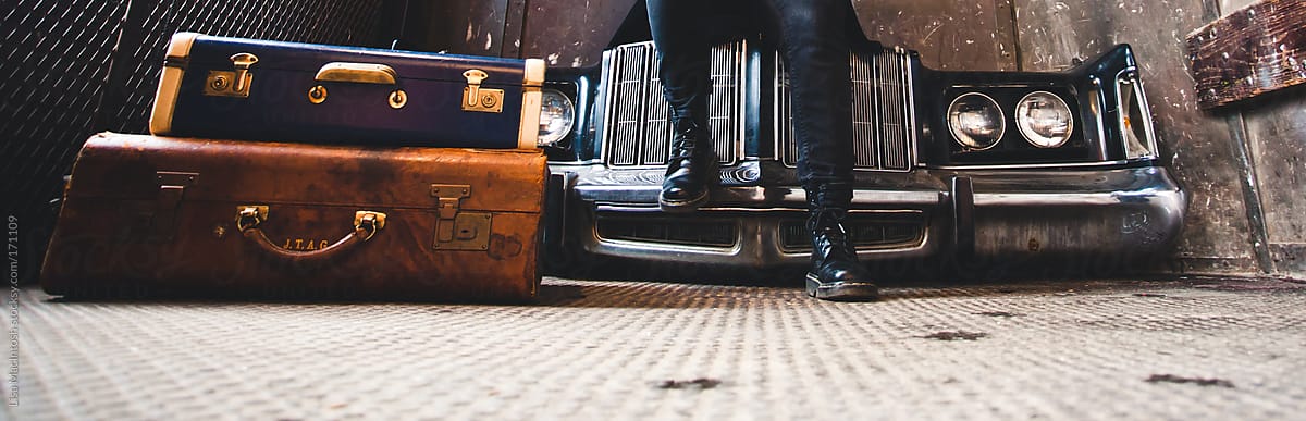 legs with punk rock boots and antique luggage in front of vintage car