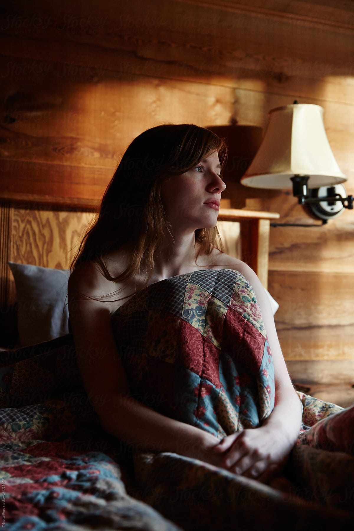 Sad woman sitting on bed in rustic log cabin thinking