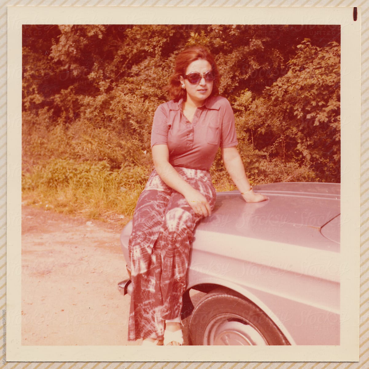 Old scanned photo of a woman on the hood of a car