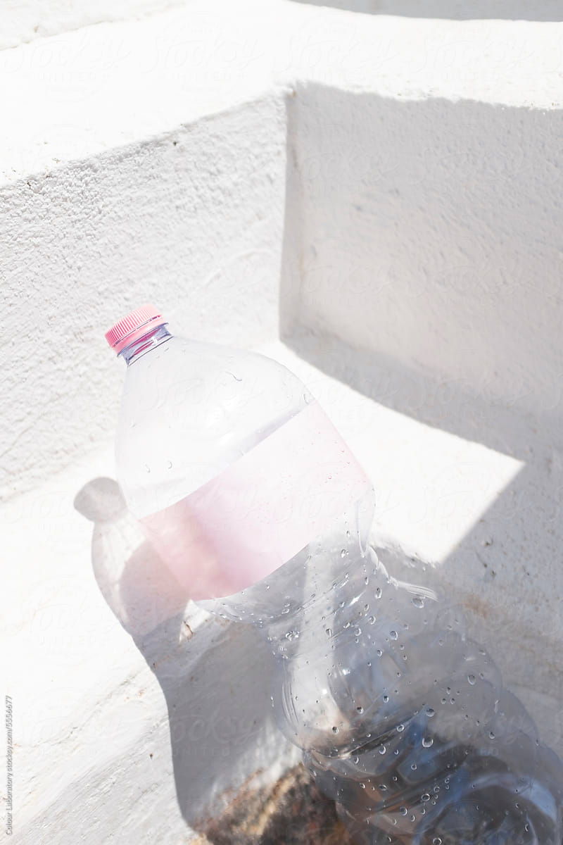 Plastic water bottle with pink etiquette laying on a wall and sunlight