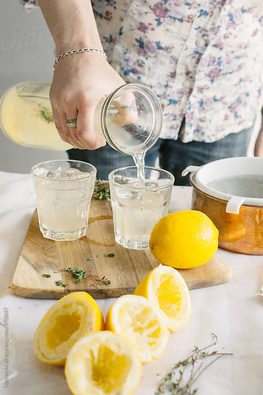 Series showing the making of homemade lemonade infused with thyme: Woman pouring homemade lemonade into a glass.